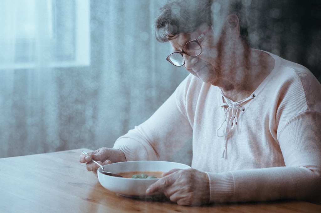 Lonely senior woman sitting at a table, dining alone thinking about socializing and nutrition. 