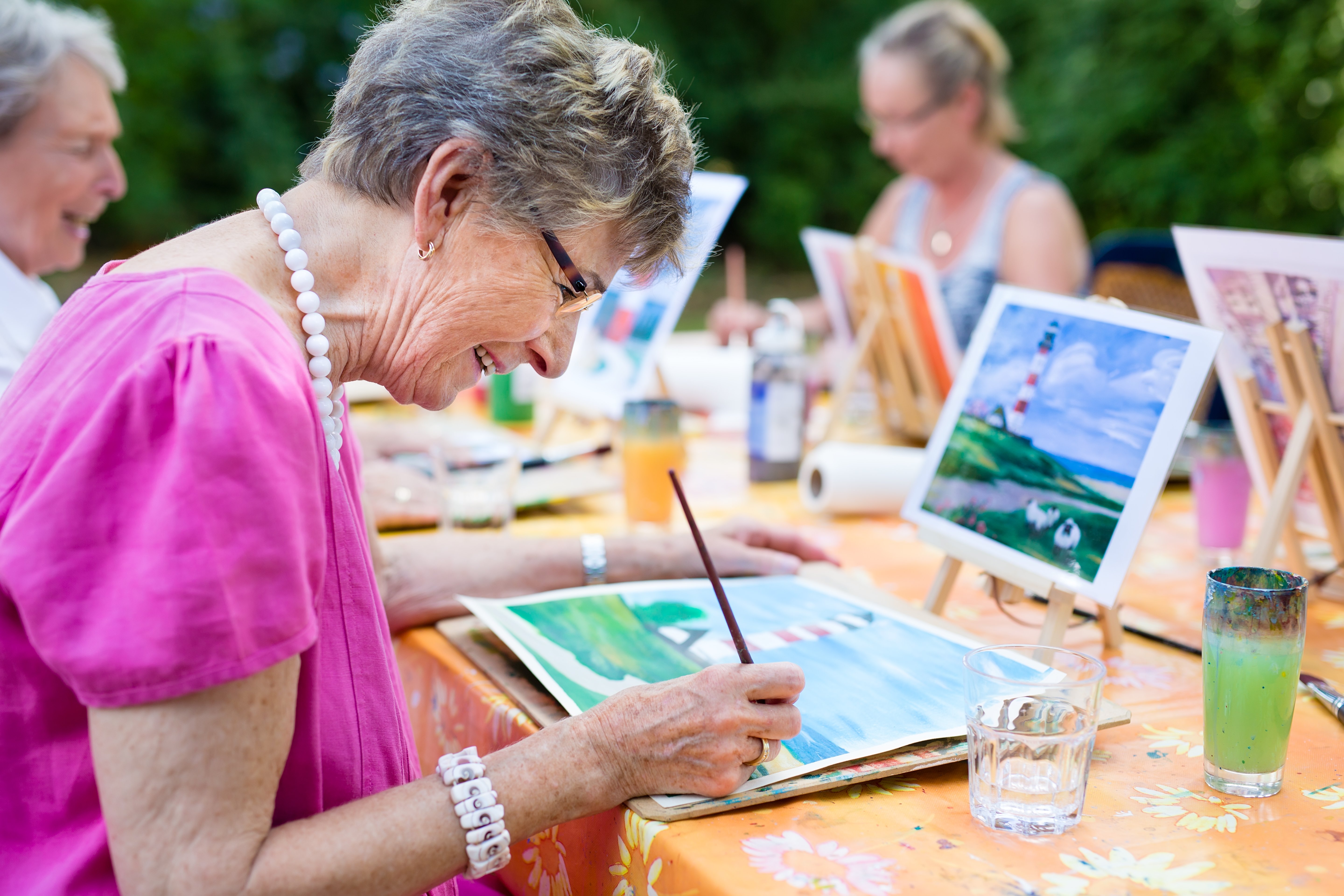 Women painting outside at a table with others and enjoying her time