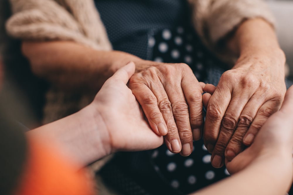 Adult child holding the hands of their senior parent, thinking about the ways to deal with their caregiver stress