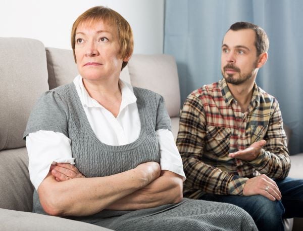 Son and mother sitting on a couch having a difficult conversation. Mother has her back to son.