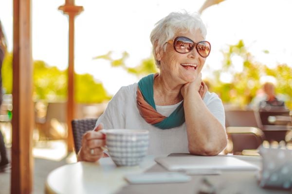 Woman sitting outside enjoying a cup of coffee while smiling and laughing