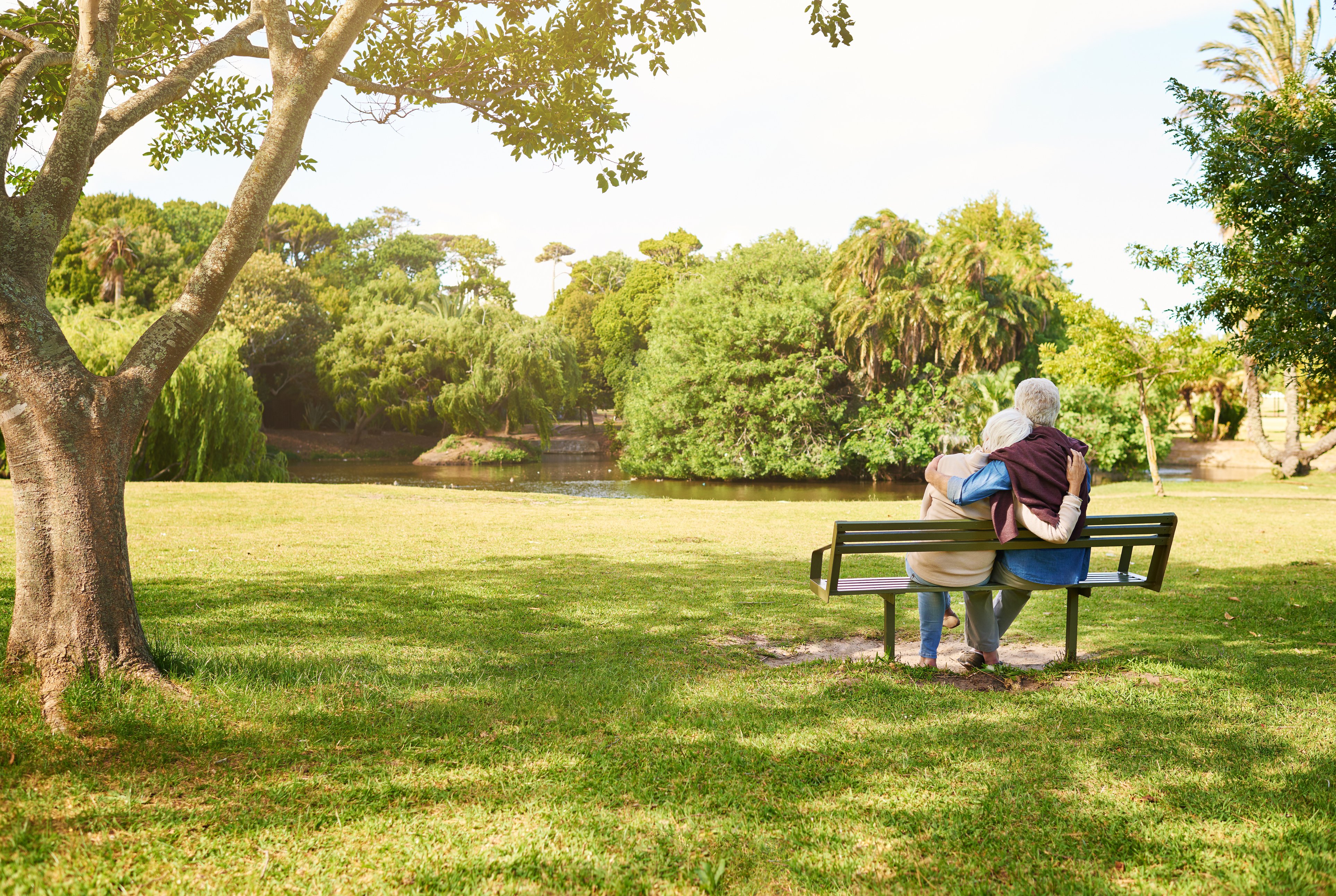 Elderly couple sitting next to one another on a park bench enjoying their time together