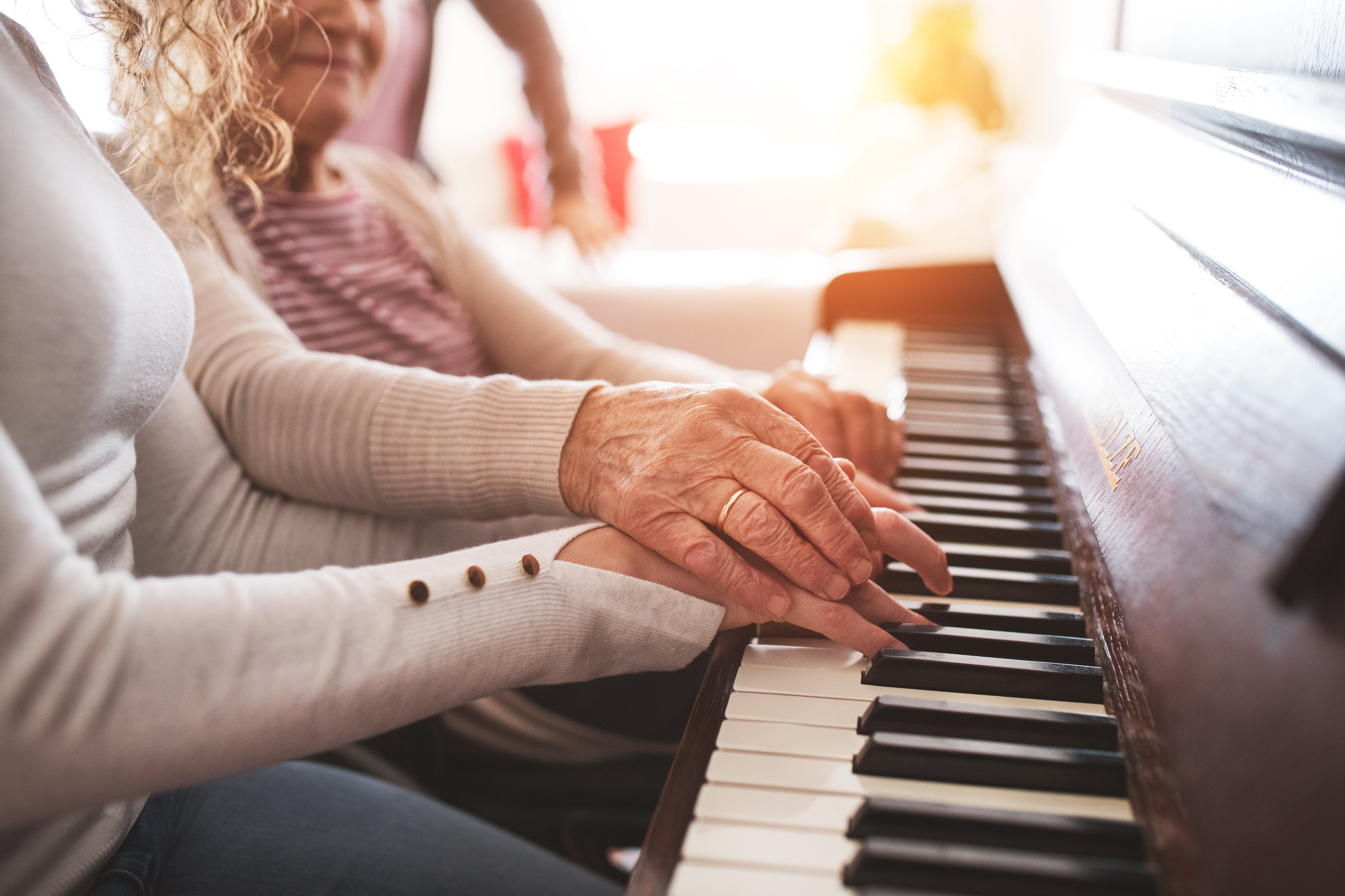Hands of a young girl and an elderly woman playing they piano
