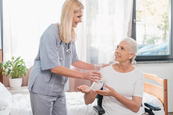 Healthcare professional giving an elderly woman her medication and water